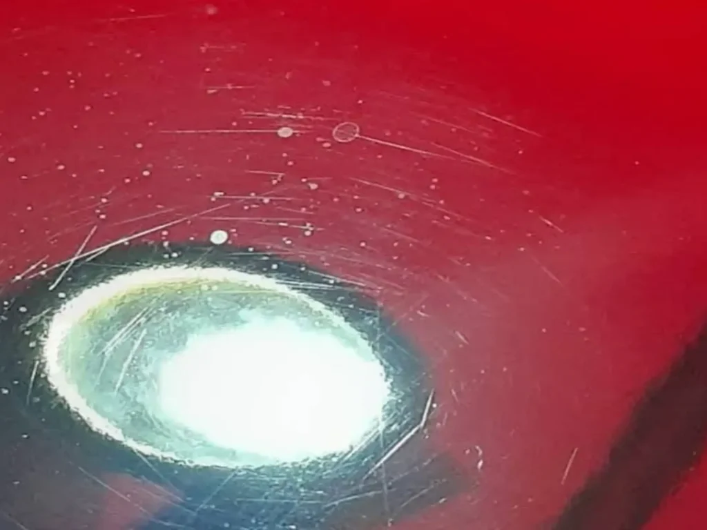 Inspection light showing swirl marks in red paint before correction