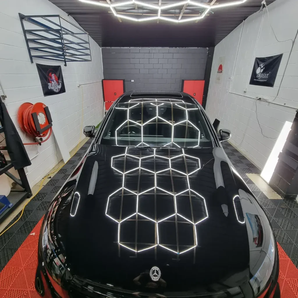 Hexagon workshop lights reflected in a freshly coated black bonnet
