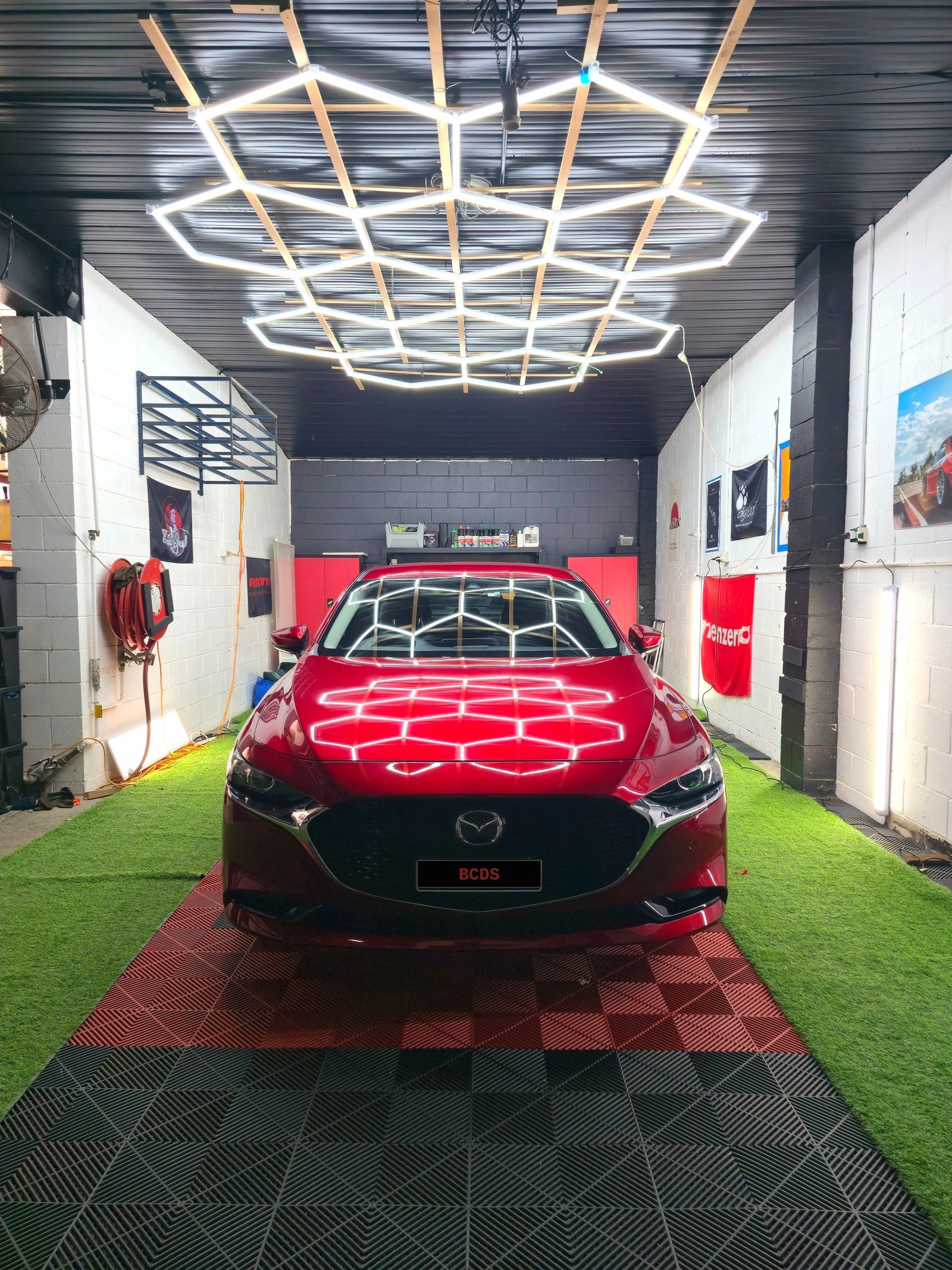 Deep red Mazda3 bonnet and windscreen reflecting the full hexagon light rig after a ceramic coating finish