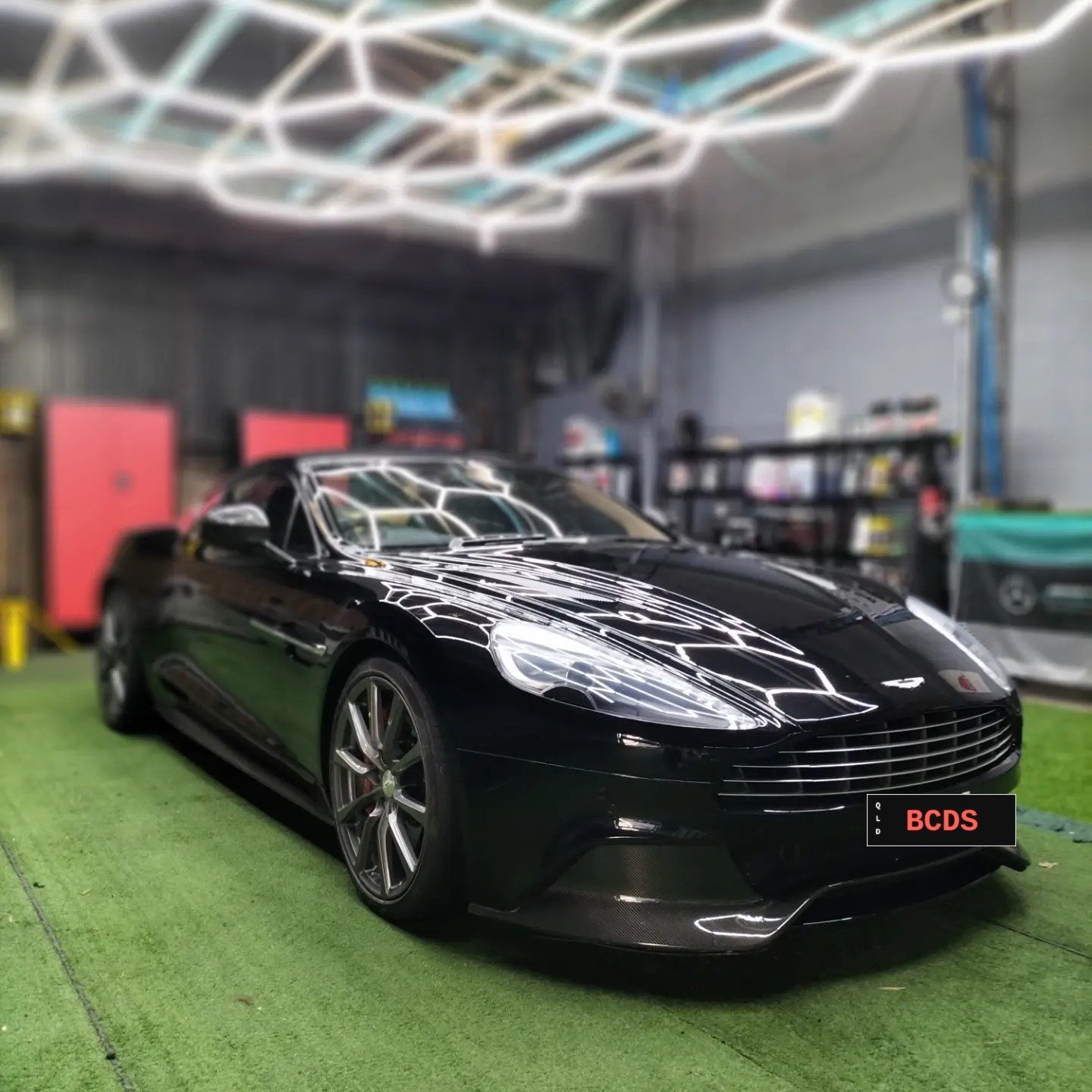Black Aston Martin finished under the workshop's hexagon light rig after paint correction