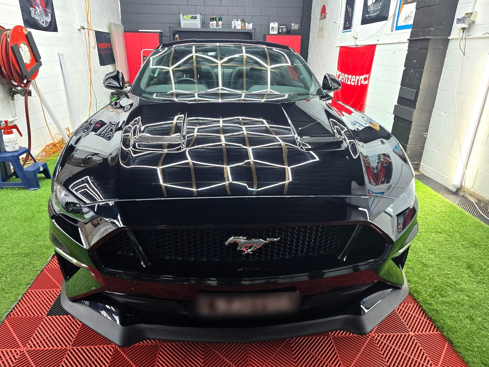 Black Ford Mustang GT front-on, the workshop's hexagon light rig reflecting across the windscreen and bonnet after specialist paint restoration